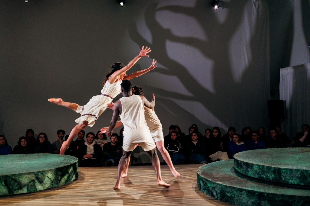 Two actors in white Edwardian undergarments are about to catch a third actor in a similar outfit, mid jump.